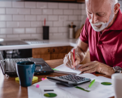 Man writing notes in book with his laptop in front of him